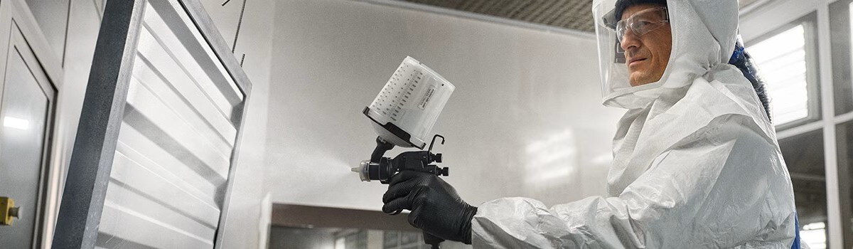 Person wearing PAPR and coveralls applying industrial paint
