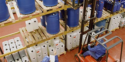 Workers in a chemical solvent warehouse checking inventory on large plastic bins of chemicals
