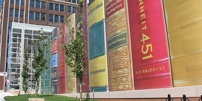 A building exterior has a large-scale building graphic wrap featuring the spines of books.
