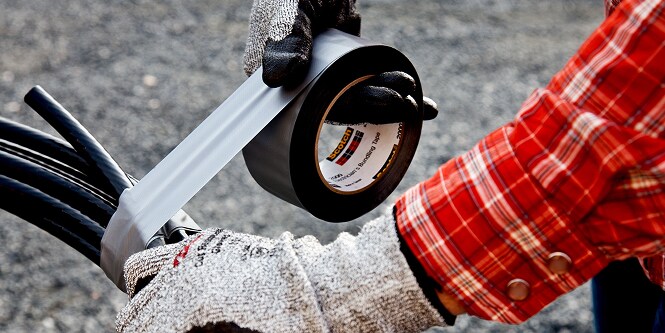 worker bundling electrical cable with tape
